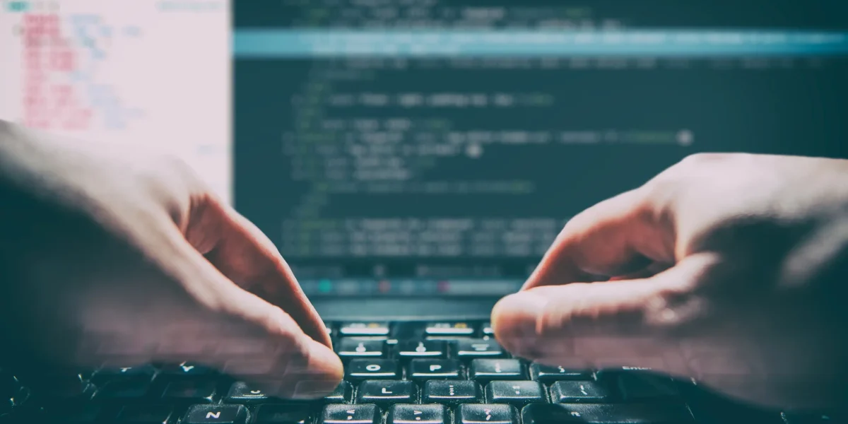 close-up of developer's hands coding, screen partially visible, selective focus